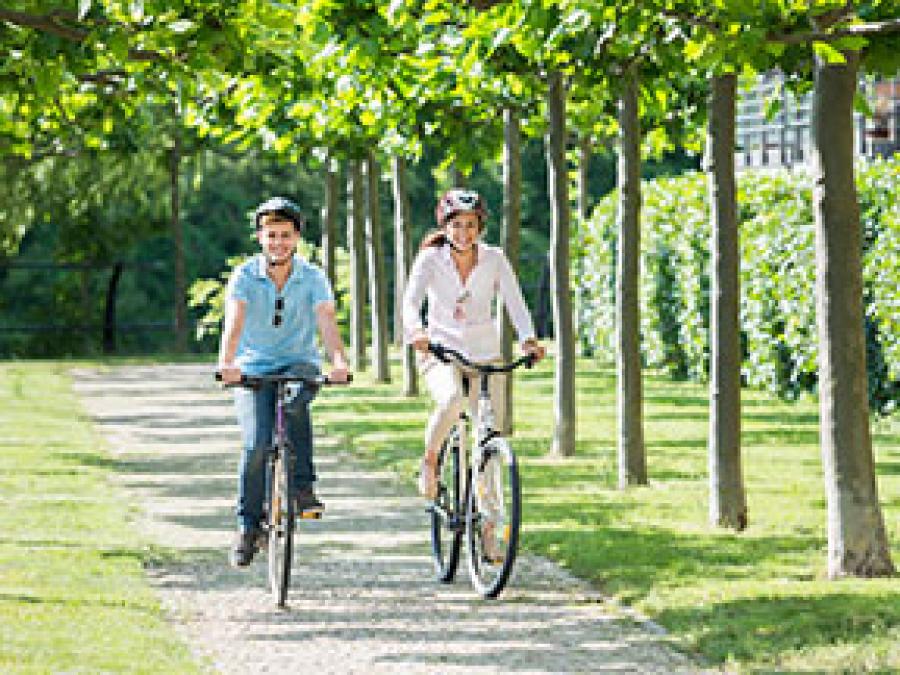 Two people riding on bikes through a park.