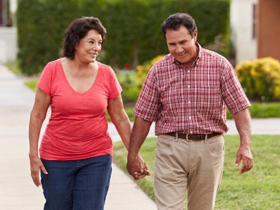 A older couple holding hands and walking on a sidewalk.